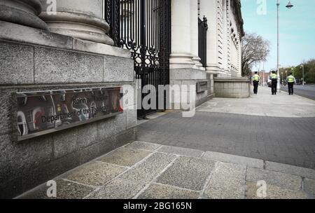 Dublin, Irland - 19. April 2020: Drei Gardai auf der leeren Straße vor dem Amt des Premierministers in Regierungsgebäuden. Stockfoto