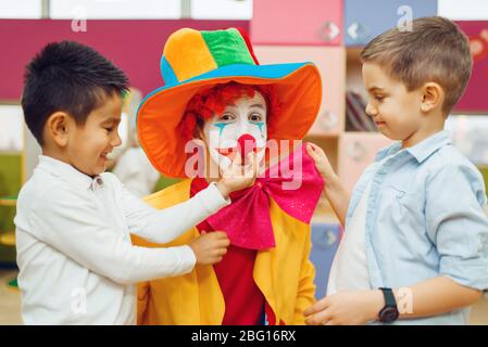 Kleiner fröhlicher Junge berührt die Nase des roten Clowns Stockfoto