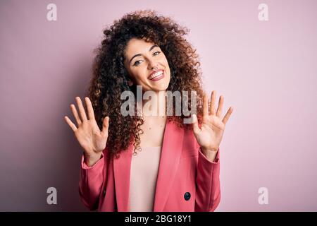 Junge schöne Geschäftsfrau mit lockigen Haaren und Piercing trägt elegante Jacke zeigt und zeigt mit den Fingern Nummer zehn beim Lächeln confid Stockfoto