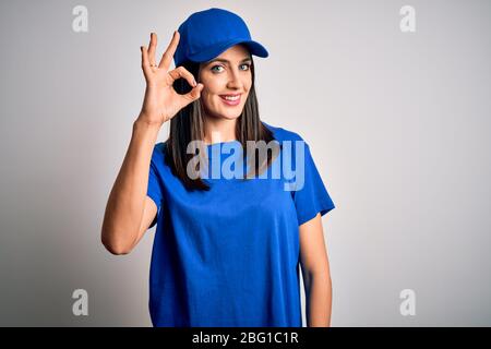 Junge Lieferfrau mit blauen Augen tragen Kappe über blauem Hintergrund lächelnd positiv tun ok Zeichen mit Hand und Finger stehen. Erfolgreich Express Stockfoto