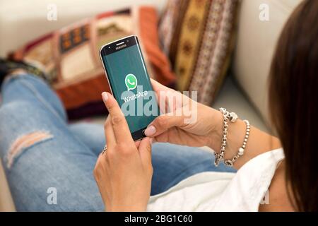 Junge Frau im Sessel mit einem Smartphone mit WhatsApp auf dem Bildschirm. ROSARIO, ARGENTINIEN - 28. OKTOBER 2017 Stockfoto