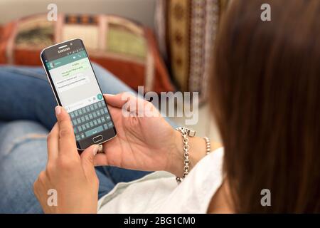 Junge Frau im Sessel mit einem Smartphone mit whatsapp-Chat auf dem Bildschirm ausruhen. ROSARIO, ARGENTINIEN - 28. OKTOBER 2017. Stockfoto