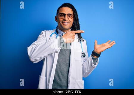 Junger afroamerikanischer Arzt mit Dreadlocks, Stethoskop und Brille, erstaunt und lächelnd zur Kamera, während er mit Hand und Poin vorstellt Stockfoto