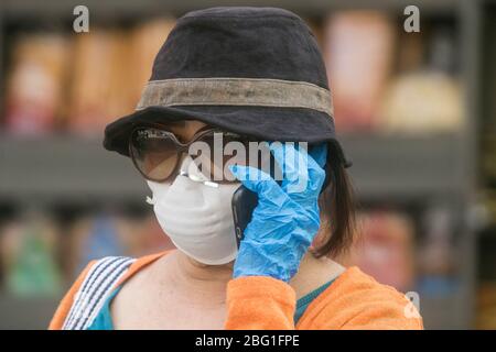 Beirut, Libanon. 20. April 2020. Eine Frau, die während der Coronavirus-Pandemie eine chirurgische Maske und Handschuhe gegen Covid-19-Infektionen trägt, während sie ein Mobiltelefon hält. Der Libanon bleibt bis zum 26. April 2020 in der Blockierung, da die Regierung die Bürger dringend aufgefordert hat, zu Hause zu bleiben und nur für wichtige Geschäfte zu gehen. Kredit: amer Ghazzal/Alamy Live News Stockfoto