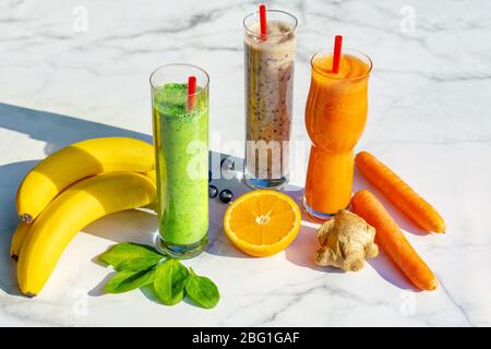 3 verschiedene Arten von Smoothies mit Zutaten auf Marmortisch Hintergrund Gigner Banane Heidelbeere Spinat Karotte. Stockfoto