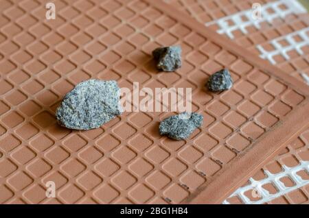 Keramikfliesen und Schotter Nahaufnahme. Eine detailreiche Aufnahme von vier Schutt-Steinen auf der Rückseite einer Keramikfliesen. Baumaterialien. Selektiver Fokus. Stockfoto