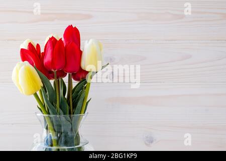 Rote und gelbe Tulpen in einer Glasvase auf hellem Holzhintergrund. Geschenkkarte mit Textraum, Modell mit leerem Platz. Rahmen mit Blumenmuster für den Urlaub Stockfoto