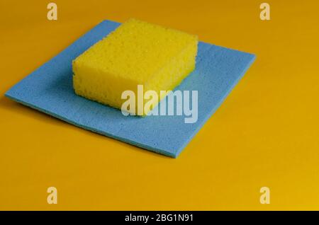 Küchenschwamm und blaue Reinigungstronbe auf gelb. Zubehör zum Spülen und Reinigen. Gewerbliche Reinigungsfirma. Selektiver Fokus. Nahaufnahme Stockfoto