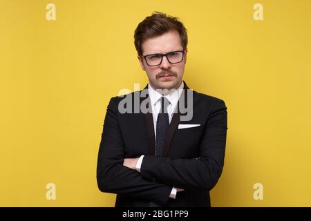 Junger seriou Geschäftsmann steht gegen die Wand mit gekreuzten Armen. studio auf gelbe Wand geschossen Stockfoto