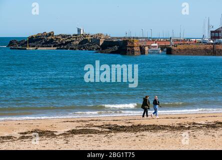 North Berwick, East Lothian, Schottland, Großbritannien. April 2020. UK Wetter: Sonnenschein und ein völlig klarer blauer Himmel in der Küstenstadt aber die schönen Strände sind fast menschenleer, wobei die wenigen Menschen, die Sport treiben, eine angemessene soziale Distanz beibehalten. Zwei Frauen gehen am Ufer entlang Stockfoto