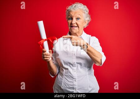 Senior schöne Studentin Frau mit Diplom stehen über isoliert roten Hintergrund sehr glücklich zeigen mit Hand und Finger Stockfoto