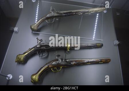 Drei verzierte antike Feuersteinpistolen mit dekorativen Metallarbeiten, die auf einer Glaswandhalterung in einer Museumsausstellung ausgestellt sind. Stockfoto