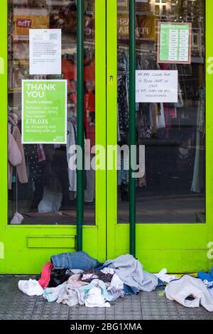 Während der Londoner Schließung, die aufgrund der Verbreitung von Covid-19, 19. April 2020, stattfand, stapelten sich die Kleidungsstücke vor dem geschlossenen Barnardo's Charity Shop in Brixton Stockfoto