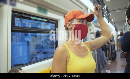 Frau fährt kaukasische Fahrt im überirdischen Zug airtrain mit Schutzmaske. Mädchen Tourist im airtrain mit Atemschutzmaske. Personenmaske. Stockfoto