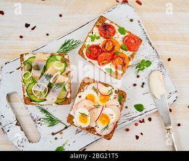 Smorrebrod: Traditionelle dänische Sandwiches. Schwarzbrot mit Hering, Ei, Tomaten, Rettich auf weißem Holztisch, Draufsicht Stockfoto