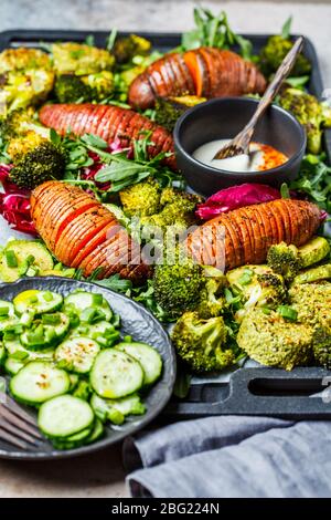 Salat mit gebackenem Gemüse und Tahini-Dressing auf Gusseisenpfanne. Gebackene Süßkartoffeln, Brokkoli und Zucchini mit Rucola. Gesundes veganes Food-Konzept. Stockfoto