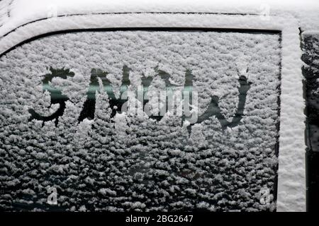 Ein Autofenster mit Schneestauben bedeckt mit dem Wort Schnee darin geschrieben Stockfoto