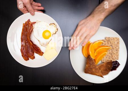 Mans Hand weg schieben eine hohe carb Platte von Lebensmitteln zugunsten einer hohen Fett ketogenen Diät Platte von Lebensmitteln. Stockfoto