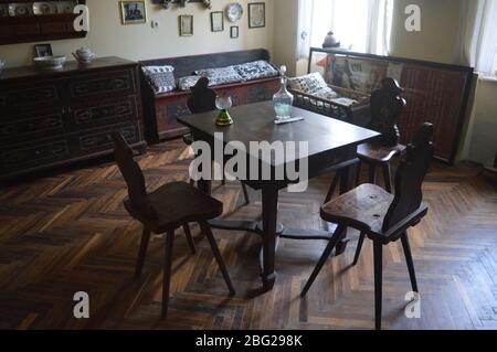 Traditionelle rustikale Einrichtung mit einem massiven Holztisch, handgeschnitzten Stühlen und Fischgrätparkettboden in einem Vintage-Zimmer. Stockfoto