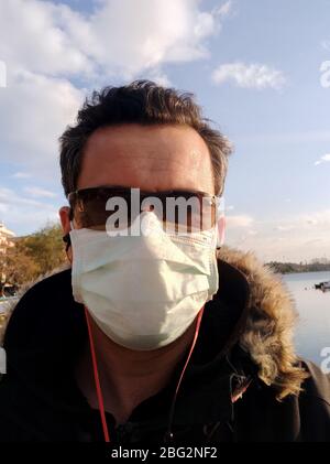 Coronavirus Covid-19 griechenland Mann mit Kopfhörer Waring Sonnenbrille und chirurgischen Schutz Maske beim Gehen draußen Stockfoto