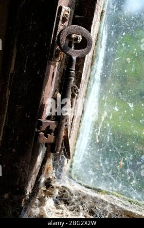 Ein alter rostiger Schlüssel hängt in einem dreckigen Fenster mit Spinnweben Stockfoto