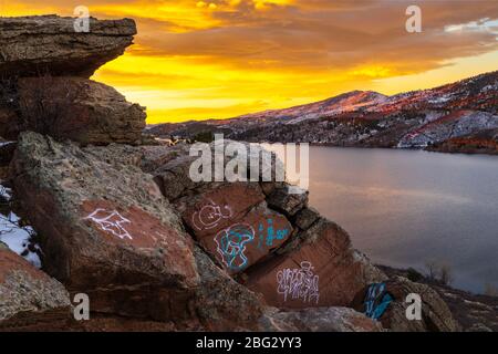 Der Himmel platzt mit Farbe auf Horsetooth Reservoir mit Graffiti auf den Felsbrocken mit Blick auf den See Stockfoto