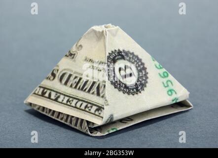 Dollar gefaltet in ägyptische Pyramide auf grauem Hintergrund Stockfoto