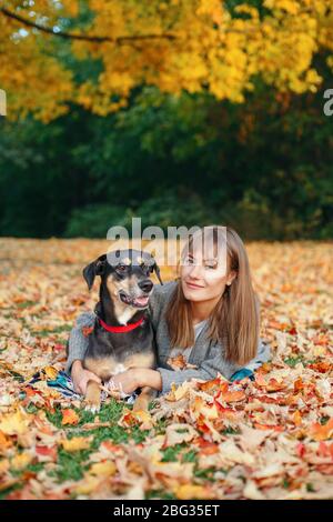 Glücklich junge kaukasische Frau auf dem Boden umarmen Hund liegen. Besitzer zu Fuß mit Haustier im Herbst Herbst Tag. Beste Freunde, die Spaß im Freien haben. Freundschaft von Brummen Stockfoto