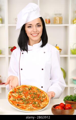 Schöne Mädchen Chef-Herd mit Pizza auf Küche Hintergrund Stockfoto