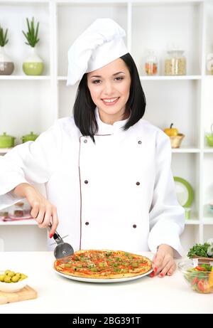 Schöne Mädchen Chef-Herd mit Pizza auf Küche Hintergrund Stockfoto