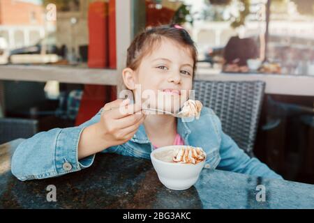 Lustige kaukasischen Vorschule Mädchen essen süßes Dessert mit Löffel im Cafe. Kind Spaß im Restaurant Terrasse Essen trinken. Gerne verbindlich Stockfoto