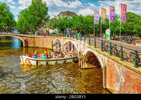 Ein Vergnügungsboot fährt unter einer Brücke mit schwulen Bannern in Amsterdam, Niederlande Stockfoto