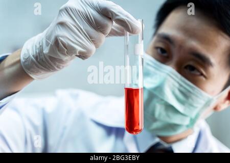Nahaufnahme eines asiatischen männlichen Wissenschaftlers in einer einheitlichen Holding-Laborflasche mit roter chemischer Lösung. Chemie, Biologische, Toxikologie, Konzept Stockfoto
