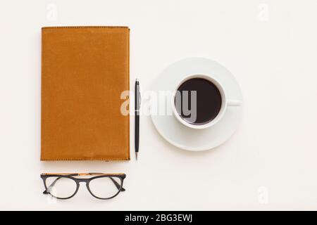 Draufsicht bei minimaler Zusammensetzung der einzelnen Kaffeetasse neben Business-Planer und schwarz-randvoll Gläser auf weißem Hintergrund, kopieren Raum Stockfoto