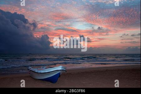 Farbenfrohe Sonnenaufgänge am Meeresstrand mit Boot im Vordergrund. Schöne Wolkenlandschaft. Stockfoto