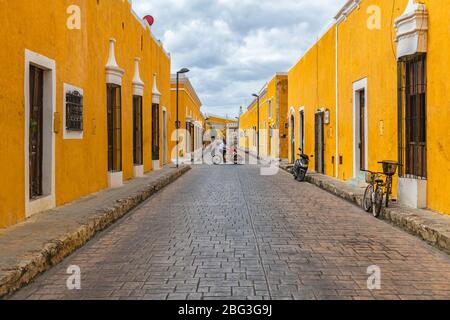 Stadtbild mit Menschen auf einem Dreirad in den bunten gelben Straßen mit kolonialer Architektur, Izamal, Mexiko. Stockfoto