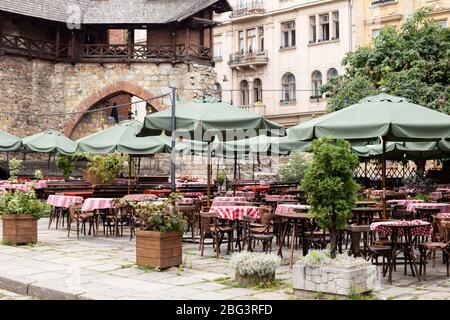 Leeres Café in der Nähe von alten Gebäuden und Burg. Viele leere Tische im Straßencafé, Holztische und Stühle, grüne Sonnenschirme. Stockfoto