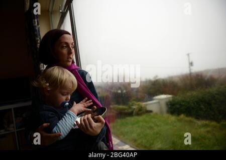 Eine junge Mutter, die an einer postnatalen Depression leidet, sitzt mit ihrem Kind an einem Fenster Stockfoto