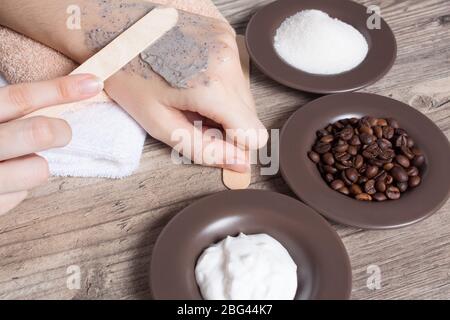 Eine Frau legt einen Spatel Kaffee hausgemachte Peeling auf ihre Hand. SPA, Schönheit. Zutaten für die Herstellung Peeling, Kaffeebohnen, Zucker, Sahne. Hautpflege. Befeuchten Stockfoto