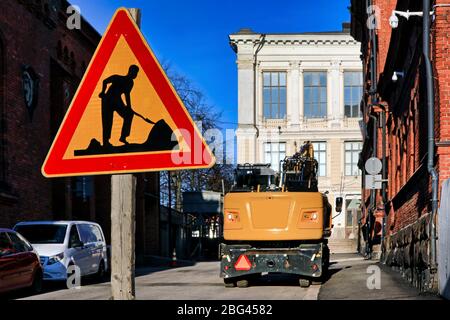 Straßenbauschild an der Stadtstraße an einem sonnigen Tag mit gelben Hydraulikbagger im Hintergrund. Keine Personen, Branding aus Bild entfernt. Stockfoto