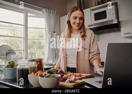 Fröhliche junge Bloggerin Browsing für Online-Rezept, um Salat von frischem Gemüse und Post auf Social Media in vlog vorzubereiten Stockfoto