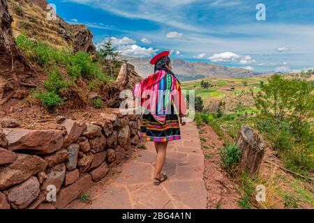 Unerkennbare Quechua Indigene Frau in traditioneller Kleidung, die entlang der alten Inka-Mauer in der Ruine von Tipon, Cusco, Peru, spazieren. Stockfoto