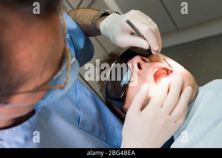 Tragen von Schutzbrillen und Mundmaske Zahnarzt untersucht die Zähne des jungen männlichen Patienten, auch mit besonderen Schutzbrille. Stockfoto