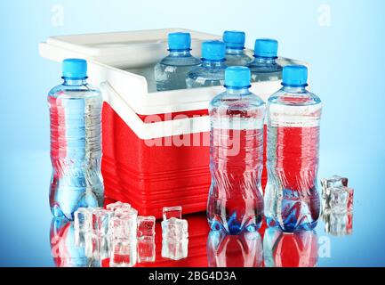 Reisekühlschrank mit Wasserflaschen und Eiswürfeln, auf blauem Hintergrund Stockfoto