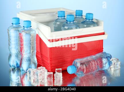 Reisekühlschrank mit Wasserflaschen und Eiswürfeln, auf blauem Hintergrund Stockfoto