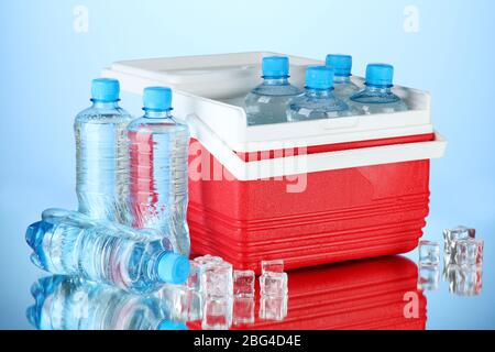 Reisekühlschrank mit Wasserflaschen und Eiswürfeln, auf blauem Hintergrund Stockfoto