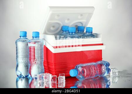 Reisekühlschrank mit Wasserflaschen und Eiswürfeln, auf grauem Hintergrund Stockfoto