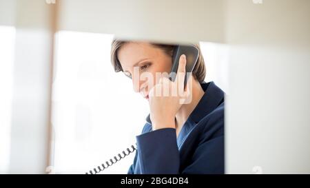 Ziemlich junge Geschäftsfrau mit kurzen Haaren Gespräch mit jemandem mit Telefon im Büro. Stockfoto