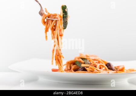 Spaghetti mit Tomatensauce und Zucchini auf einer Gabel über weißem Teller. Stockfoto