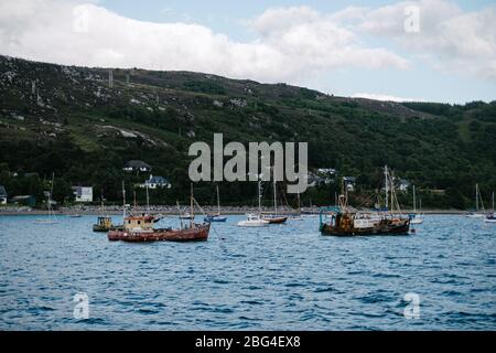 Fischerboote und Vergnügungsboote ankerten im Ullapool Hafen am Loch Broom mit den Bergen im Hintergrund. Stockfoto